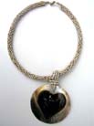 Heart shaped center of large circular pendant hanging from twisted bead necklace